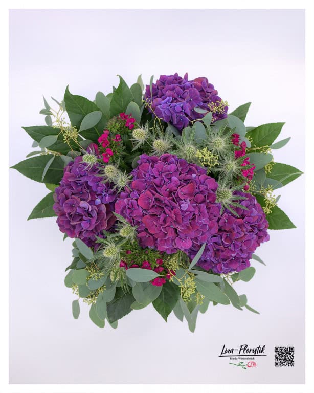 The top view of the bouquet features purple hydrangeas, red carnations and thistles, stylishly complemented by fresh eucalyptus