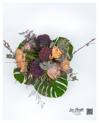 Exotic king protea, strong hydrangeas and delicate chrysanthemums, framed by eucalyptus, larch branches and monstera leaves.