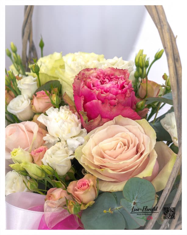 Detailed shot of a romantic flower basket with roses in soft pink, cream and strong pink - complemented with eucalyptus and lisianthus. A lovingly designed arrangement that touches the heart and eyes.