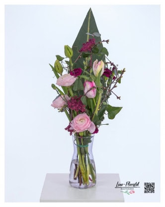 Modern bouquet with pink ranunculus, purple carnations, colored ammi and delicate tulips, combined with decorative cherry branches and a large strelitzia leaf as a background.