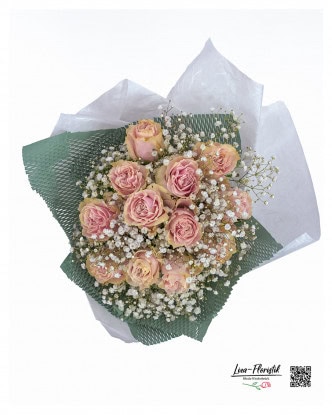 Detailed view of the bouquet with 12 pink roses from Ecuador and fine gypsophila - carefully tied, with a green net cuff and white tissue paper, this perspective shows the even arrangement and high quality of the flowers from Liza-Florist from Rheda-Wiedenbrück.