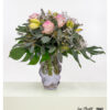 Delicate bouquet in shades of pink and cream, accented with lush greenery and subtle white details, loosely and elegantly arranged